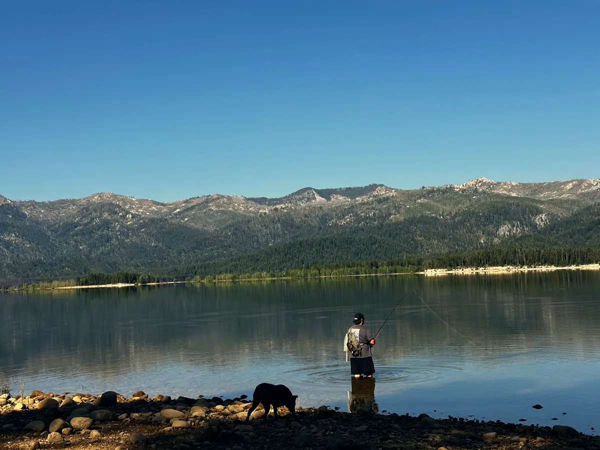 Chad fishing in a mountain lake at evening while his dog walks the rocky shore